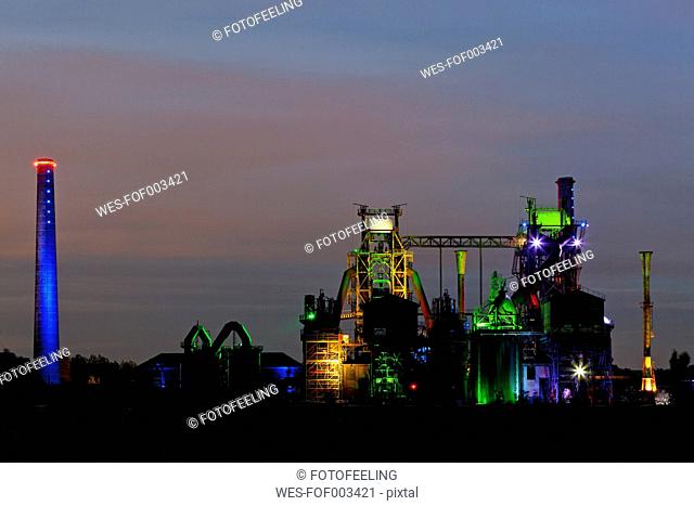 Germany, Nordrhein-Westfalen, Duisburg, Duisburg-Nord Landscape Park, View of illuminated blast furnace and smoke stacks of old industrial plant