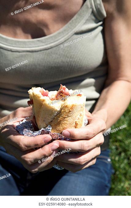 woman green color shirt blue jeans trousers with iberian ham panini sandwich bread wrapped in tin foil in her hands