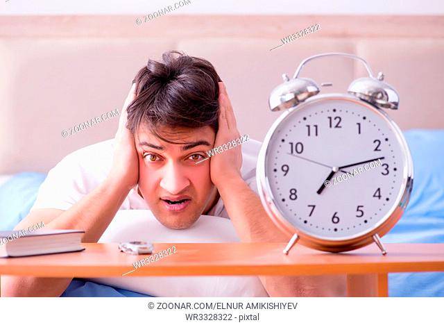 Man in bed frustrated suffering from insomnia with an alarm clock