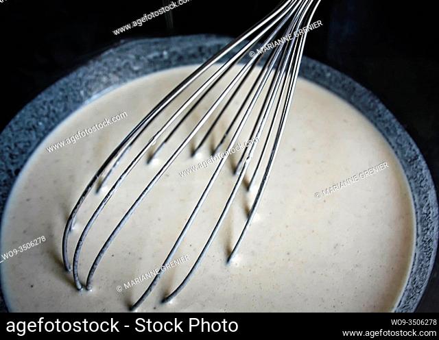 Metal whisk in a white liquid dough close up