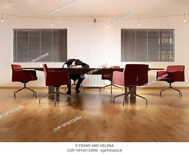 Businessman with his head in his arms at conference table. He looks like he is asleep