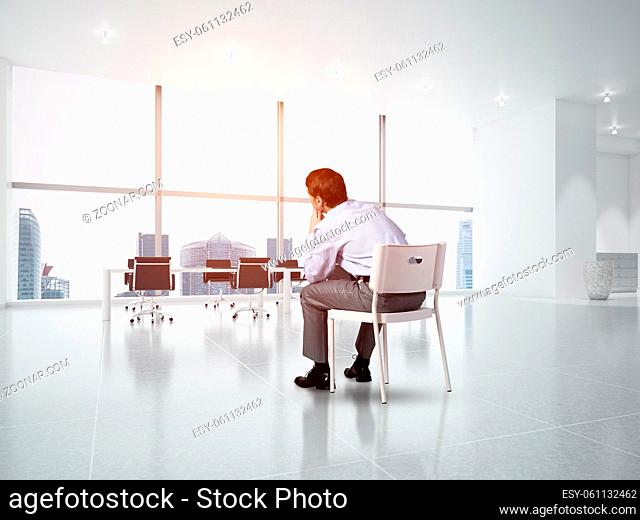 young businessman sits on an office chair, thoughtful and looking up