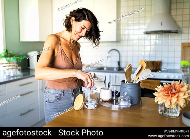 Happy woman filling glass jar at kitchen counter