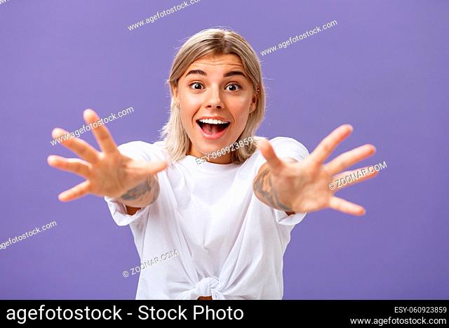 Lifestyle. Waist-up shot of amused and excited attractive stylish young woman in white t-shirt pulling hands at camera with desire smiling thrilled and happy...