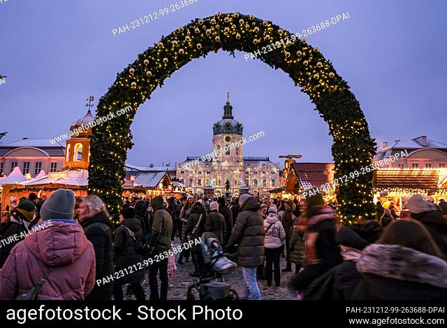 03 December 2023, Berlin: Numerous visitors can be seen at the atmospherically illuminated Christmas market at Charlottenburg Palace in the evening at dusk