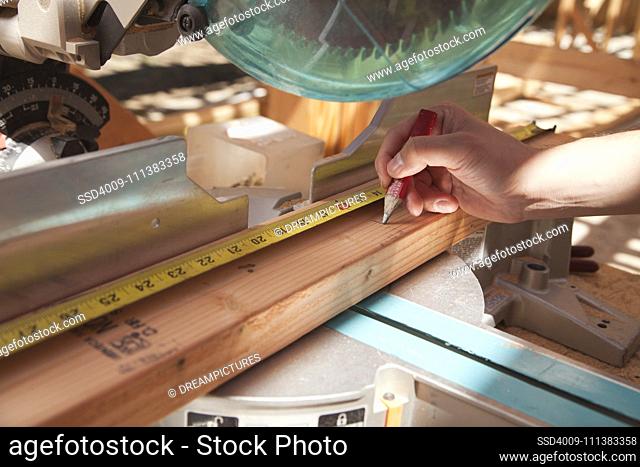 Mixed race man measuring wood on saw