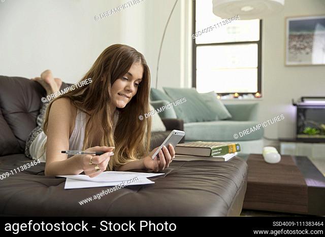 Woman using cell phone to study on sofa