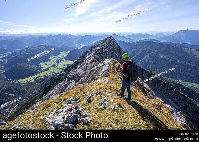 Hiker with climbing helmet, on hiking trail at a ridge, view of mountain landscape, in the back mountain ridge with peak of Seehorn, Nuaracher Höhenweg