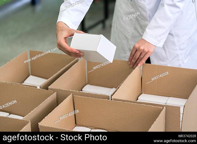 High-angle close-up view of the hands of a manufacturing worker putting packed products in cardboard boxes, before export or shipping during manual work in a...