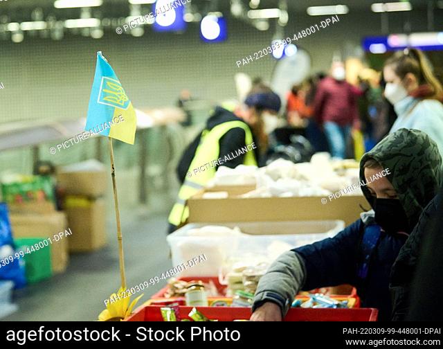 09 March 2022, Berlin: A Ukrainian flag stands on tables with life funds for the refugees from Ukraine in the main station