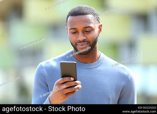 Front view portrait of a serious black man using cellphone in the street