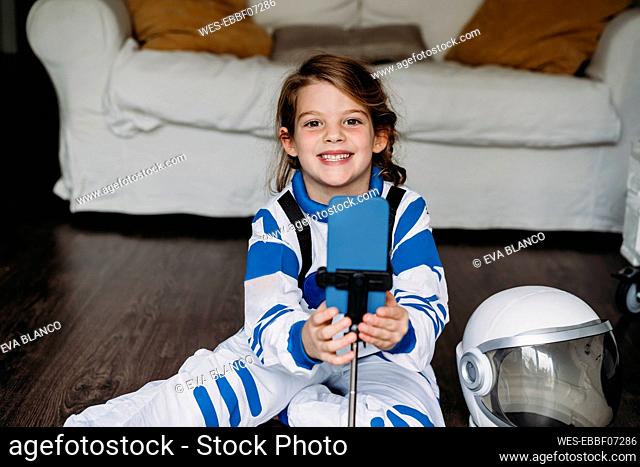 Happy girl wearing space costume with mobile phone in living room