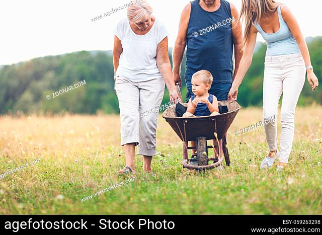 Family pushing their small child and grandchild in a wheelbarrow