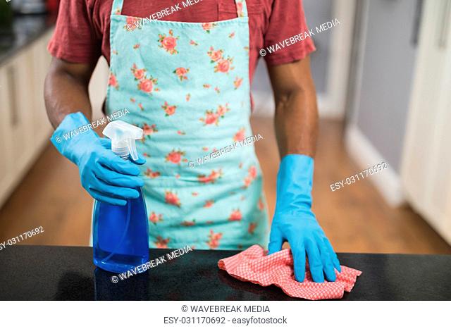 Mid section of man holding spray bottle and rag in kitchen