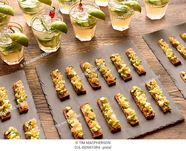 Guacamole, smoked salmon and rye bread canapes with vodka cocktail garnished with lime wedges