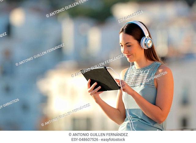 Relaxed woman browsing tablet videos in a town at sunset