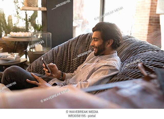 Man using mobile phone while relaxing on arm chair