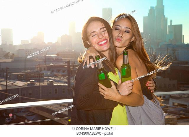 Portrait of two young women hugging at rooftop bar with Los Angeles skyline, USA
