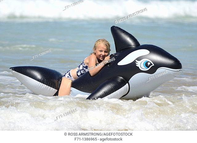 Six year old girl at the beach playing in the surf on inflatable Orca Mimiwhangata Northland, New Zealand