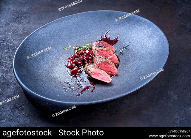 Modern style traditional wild hare back filet braised with wild berries and cherry relish souse served as close-up on Nordic design plate with copy space