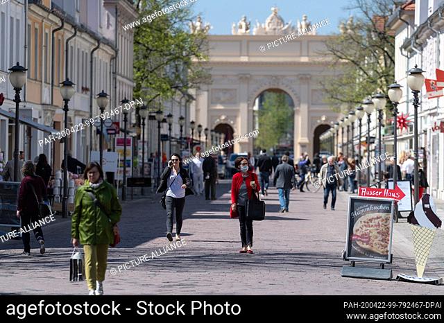 22 April 2020, Brandenburg, Potsdam: A woman with a face mask and shopping bag is walking on the shopping mile Brandenburger Straße coming from the direction of...