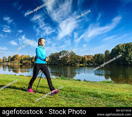 Nordic walking adventure and exercising, young woman hiking with nordic walking poles in park along river