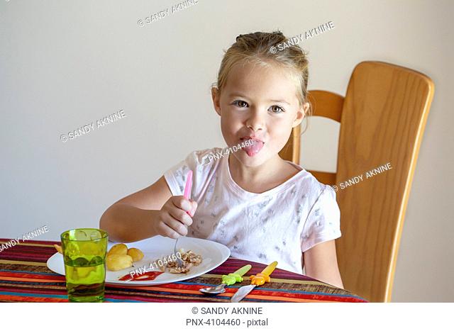 Pretty little girl at table in front of her plate trying to pull her tongue out