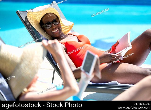 Happy senior women friends relaxing and sunbathing at sunny poolside