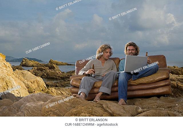 men with laptop and beer on couch, beach