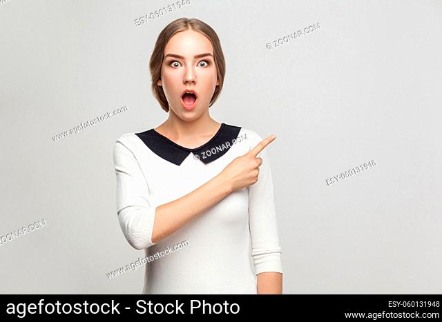 Boss pointing finger at copy space, and looking at camera with shocked face and big eyes. Studio shot, gray background