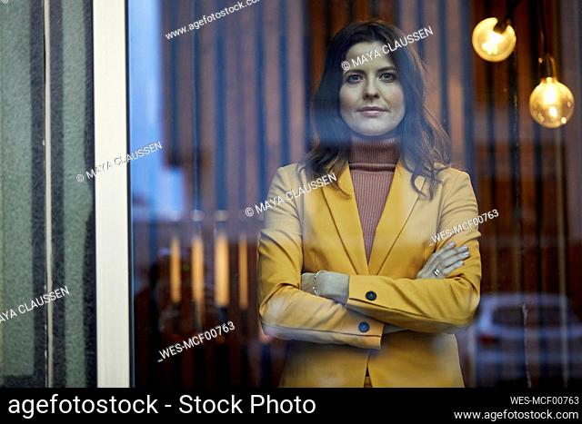 Portrait of confident businesswoman wearing yellow suit standing behind windowpane