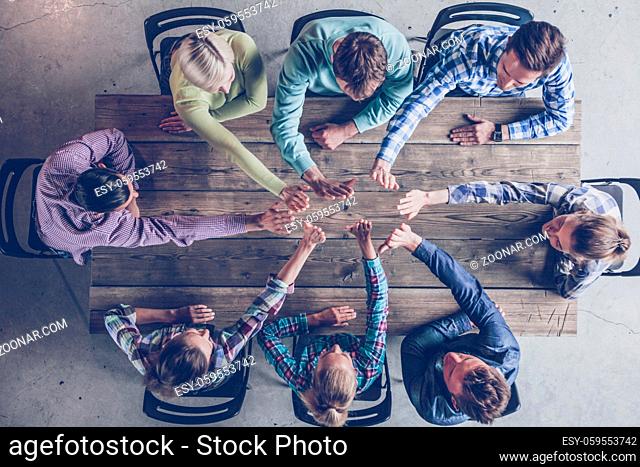 Business people team giving high five gesture and sitting at table in office top view