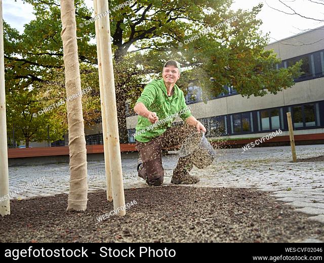 Happy young gardener scattering grass seeds
