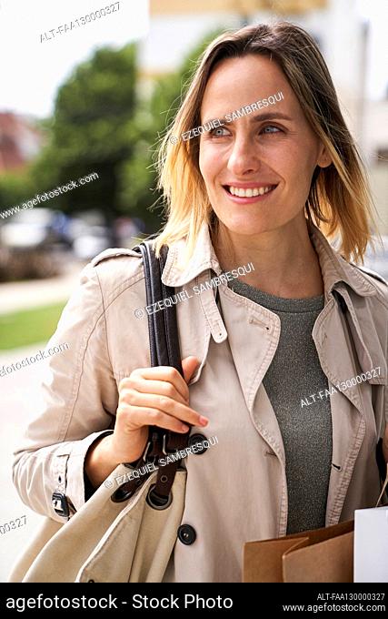 Mid-shot of smiling woman holding her handbag while walking in the street