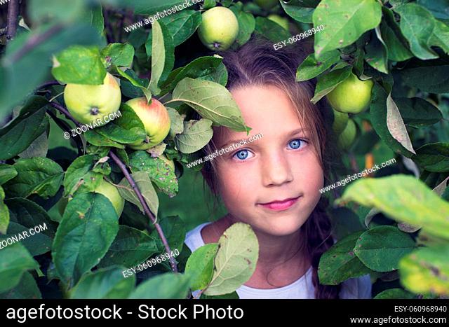 cute girl among apple tree branches full of fruits