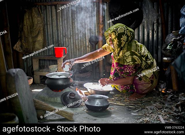 A woman is cooking rice balls on a traditional charcoal-burning clay stove at Narsingdi, Bangladesh