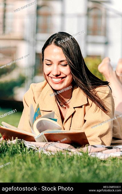 Happy beautiful woman reading book lying at park on sunny day