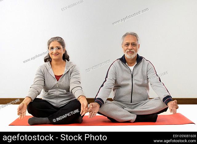 AN OLD COUPLE SITTING TOGETHER AND SMILING WHILE MEDITATING