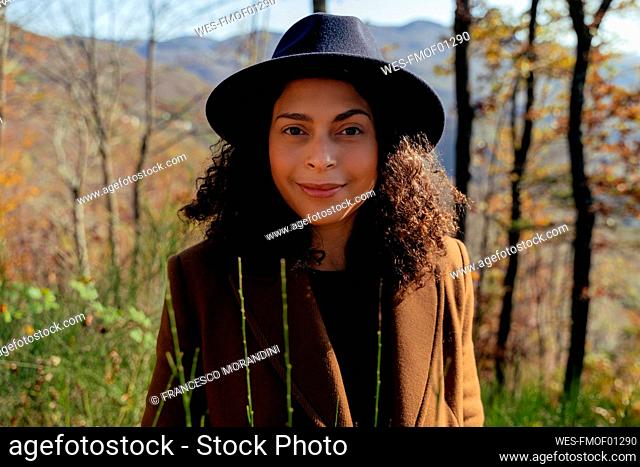 Beautiful female in hat smiling while standing in forest