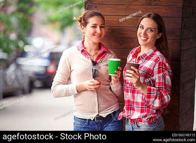 Toned picture of pretty ladies drinking cups of coffee outdoors. Happy smiling girls communicating or talking near restaurant or cafe