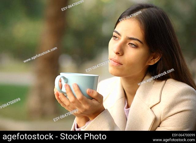 Pensive woman in winter holding coffee mug in a park