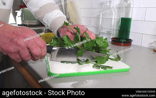 A cook chops parsley in the kitchen on a cutting board