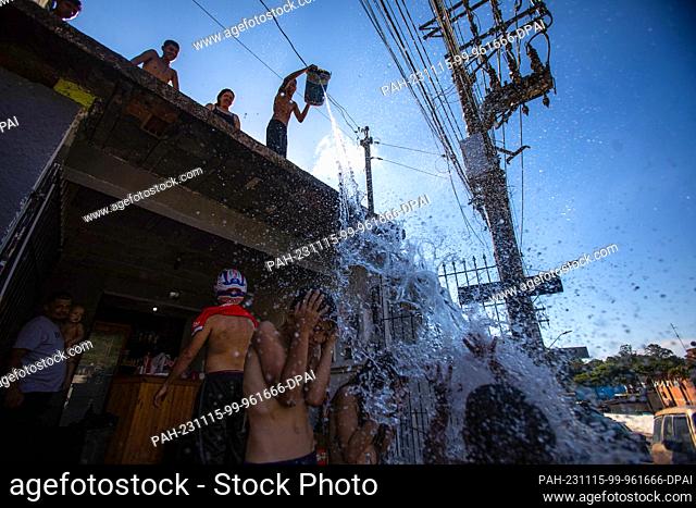 15 November 2023, Brazil, Sao Paulo: Children throw water with a bucket from a roof during an extreme heatwave. Even before the start of summer in the southern...