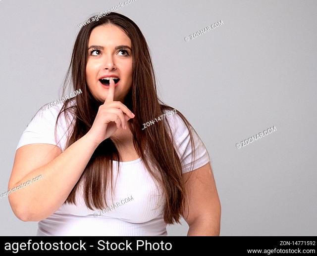 Plus Size Girl holds finger at mouth urging to keep silence