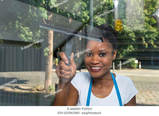 African Woman Cleaning Glass With Rubber Window Cleaner From Outside
