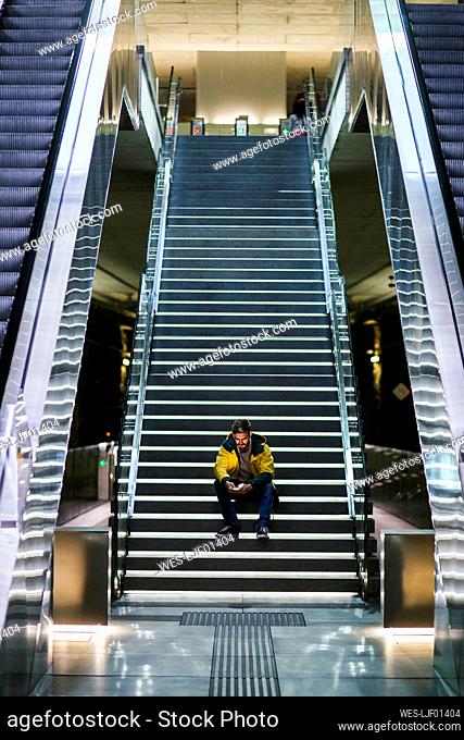 Man sitting on stairs in subway station using cell phone