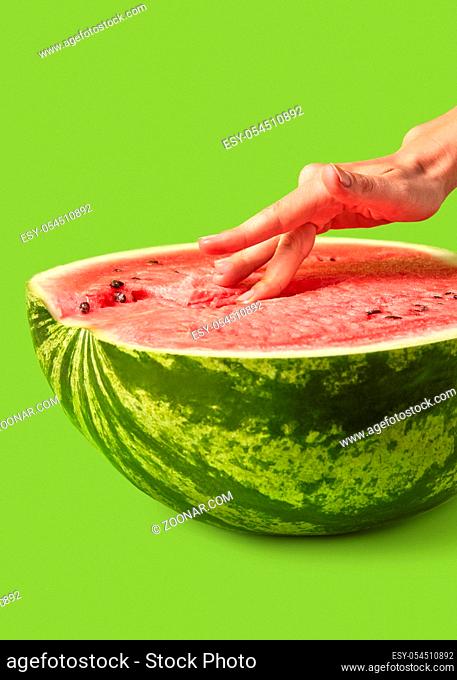 Woman's fingers touch inside organic ripe fresh watermelon's puree on a lawn green background with copy space. Easy eroticism. Sex concept