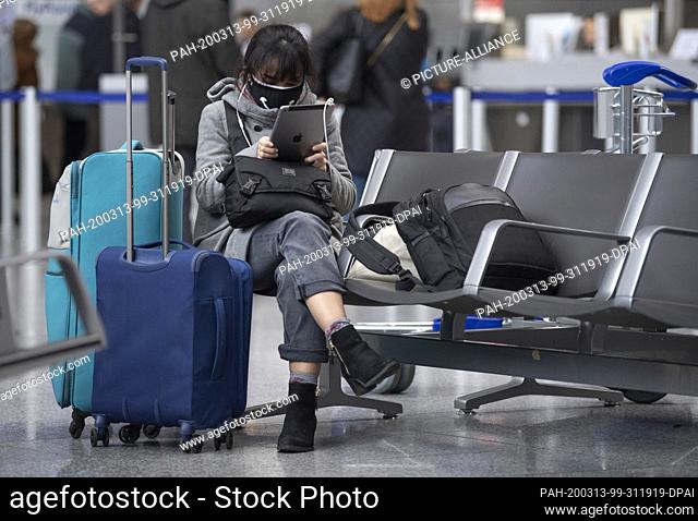 13 March 2020, Hessen, Frankfurt/Main: With a large face mask this woman protects herself in the waiting area of the terminal