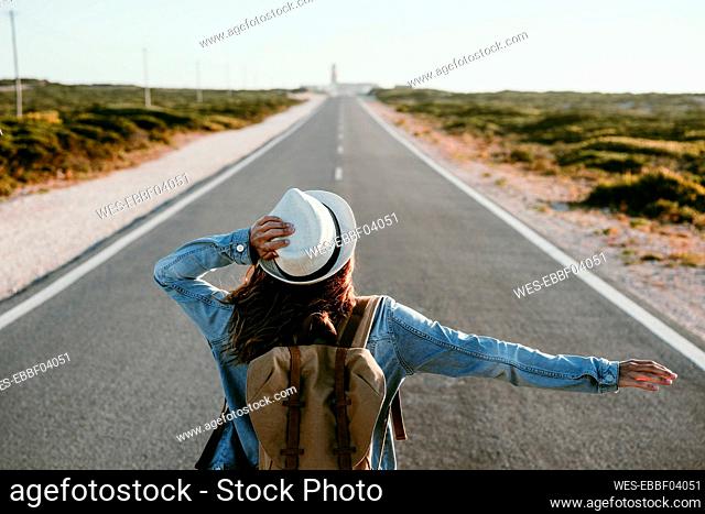 Woman holding hat while standing on road