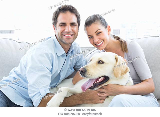 Smiling couple petting their yellow labrador on the couch